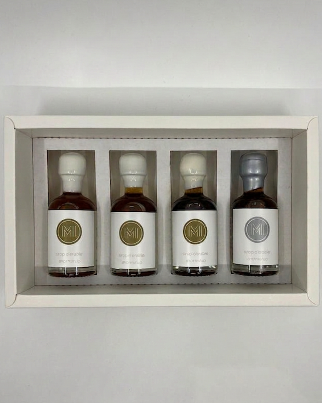 Four bottles of maple syrup, 3 with white wax plus one with grey wax, in a decorative box with a plain background