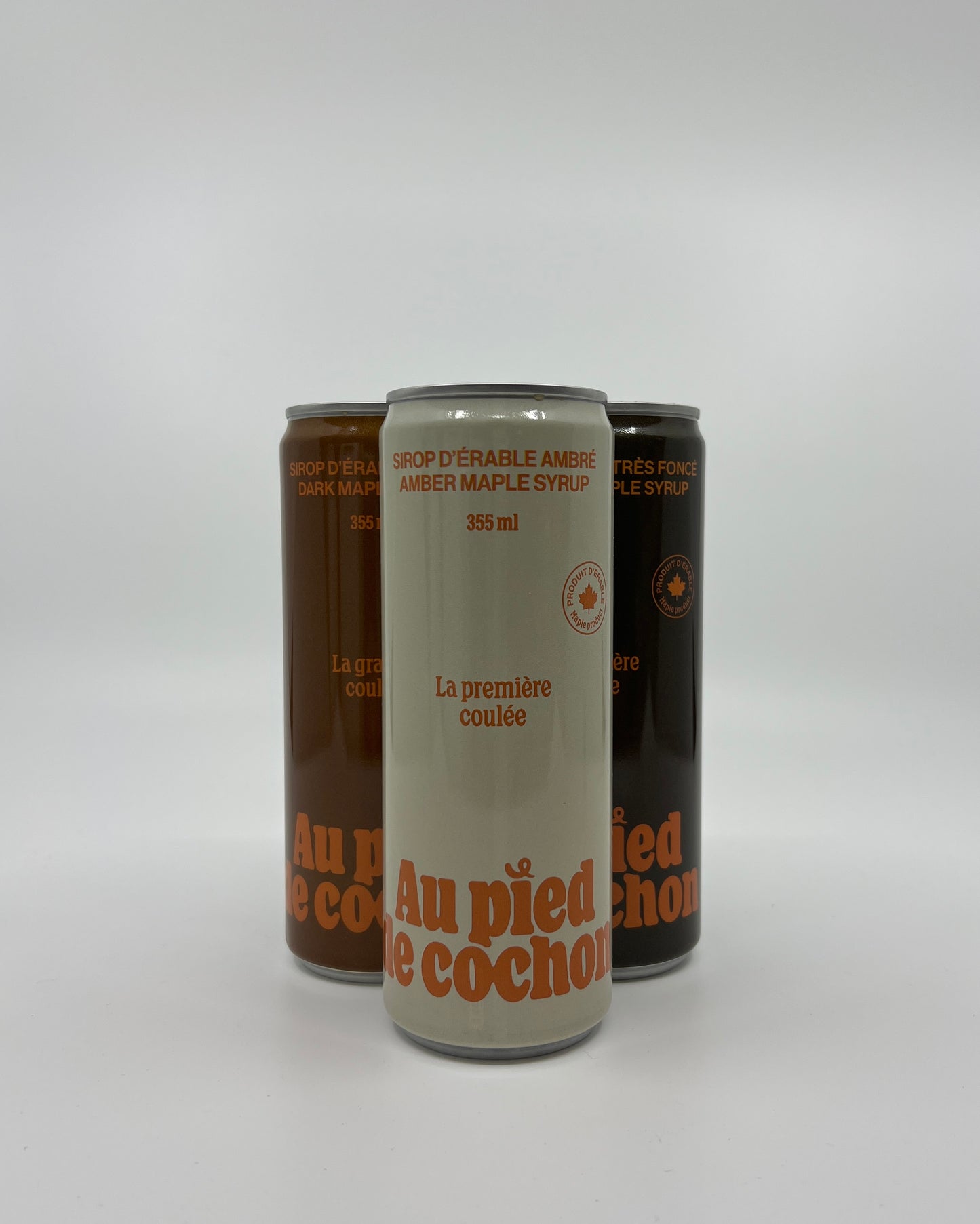 a bottle of amber maple syrup 355ml named la grande coulée without lid on a white background in front of 2 other bottles of the same style but different colors.