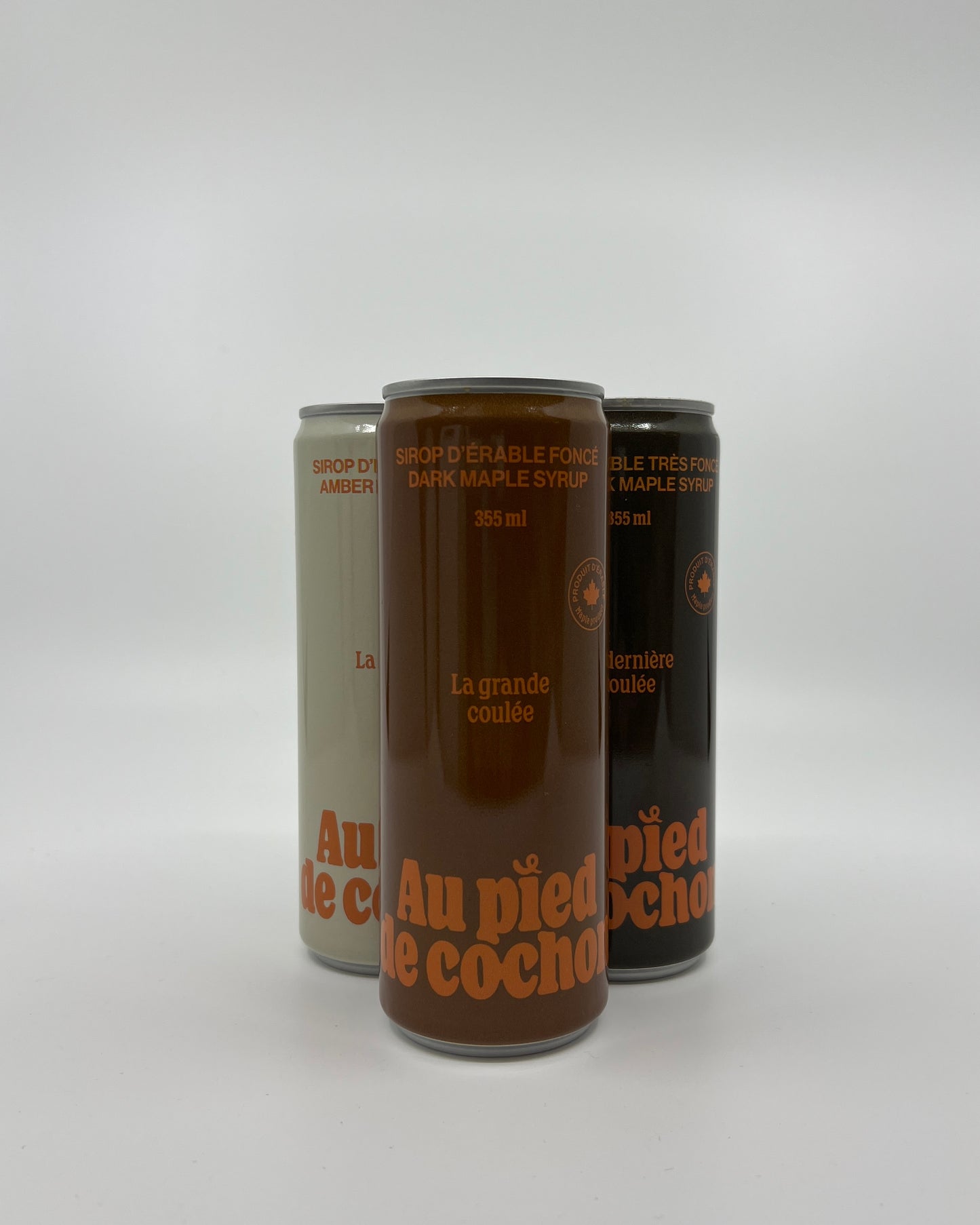 a bottle of dark maple syrup 355ml named la grande coulée without lid on a white background in front of 2 other bottles of the same style but different colors.