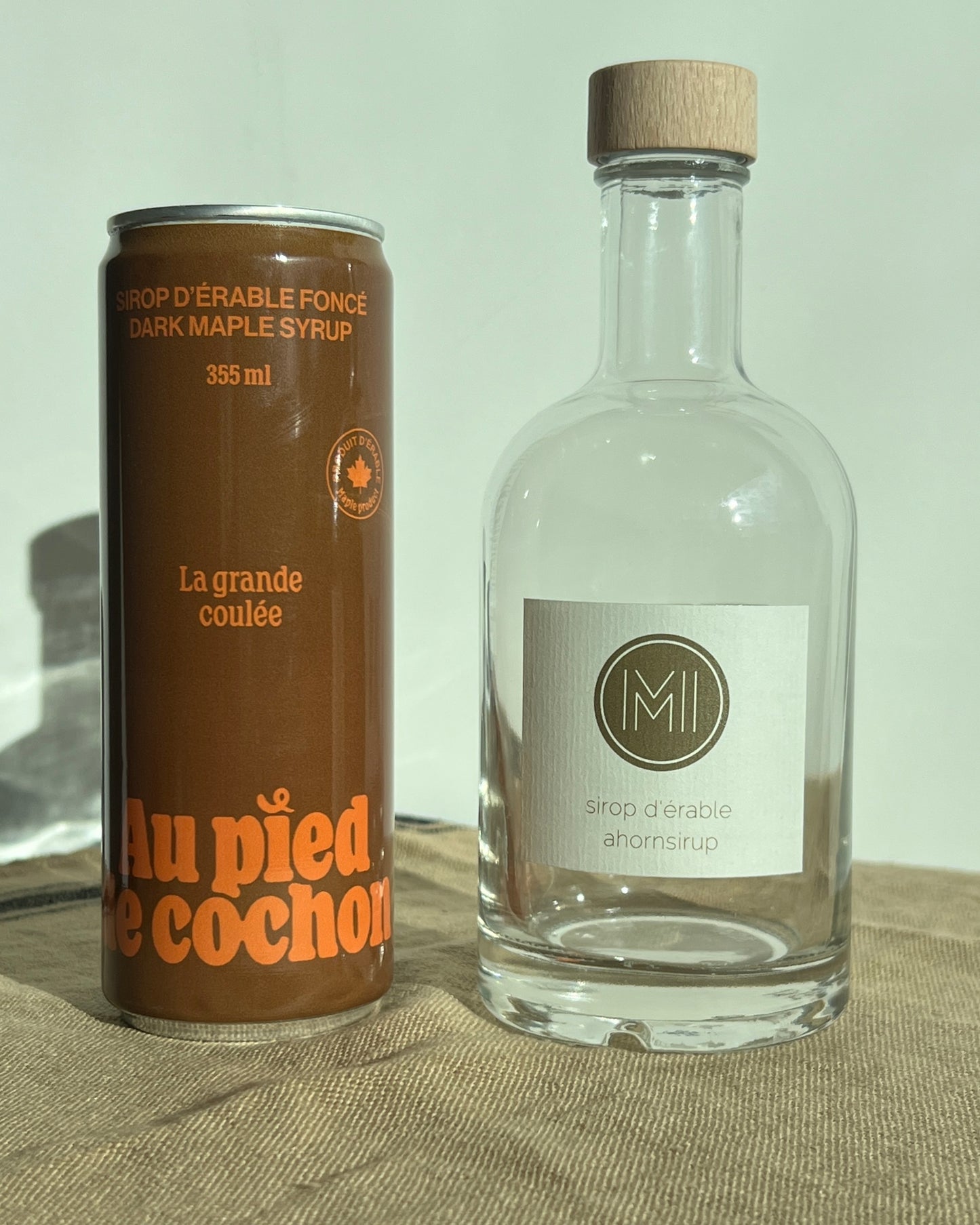 a bottle of dark maple syrup 355ml named la grande coulée side by side with glass jar on a table cloth