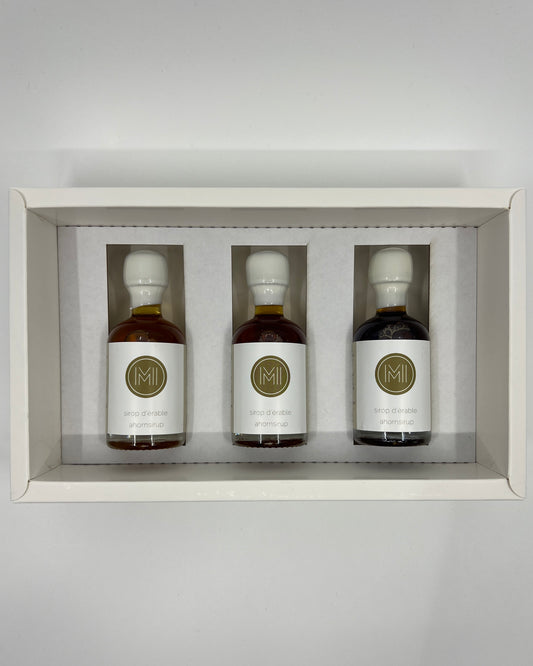 3 side by side small bottles of maple syrup presented in a white box with insert on a white background