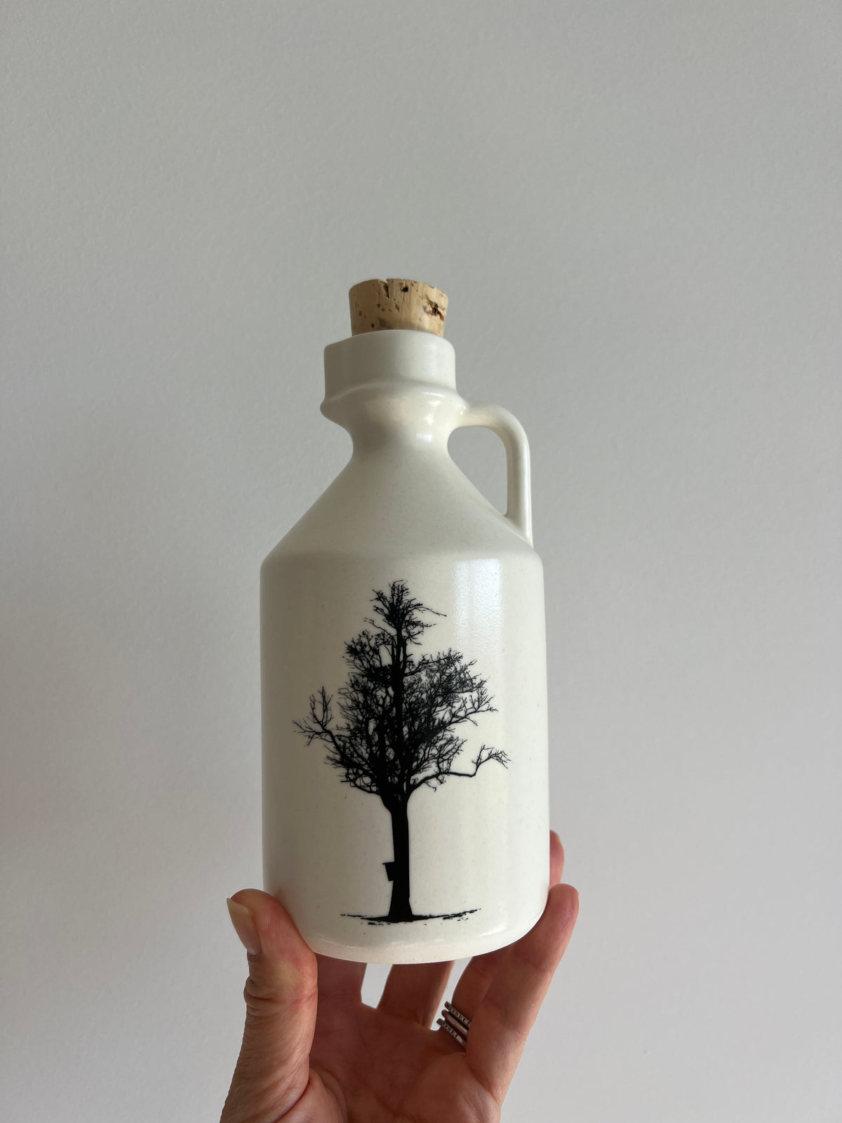 hand holding a ceramic jar with a maple tree