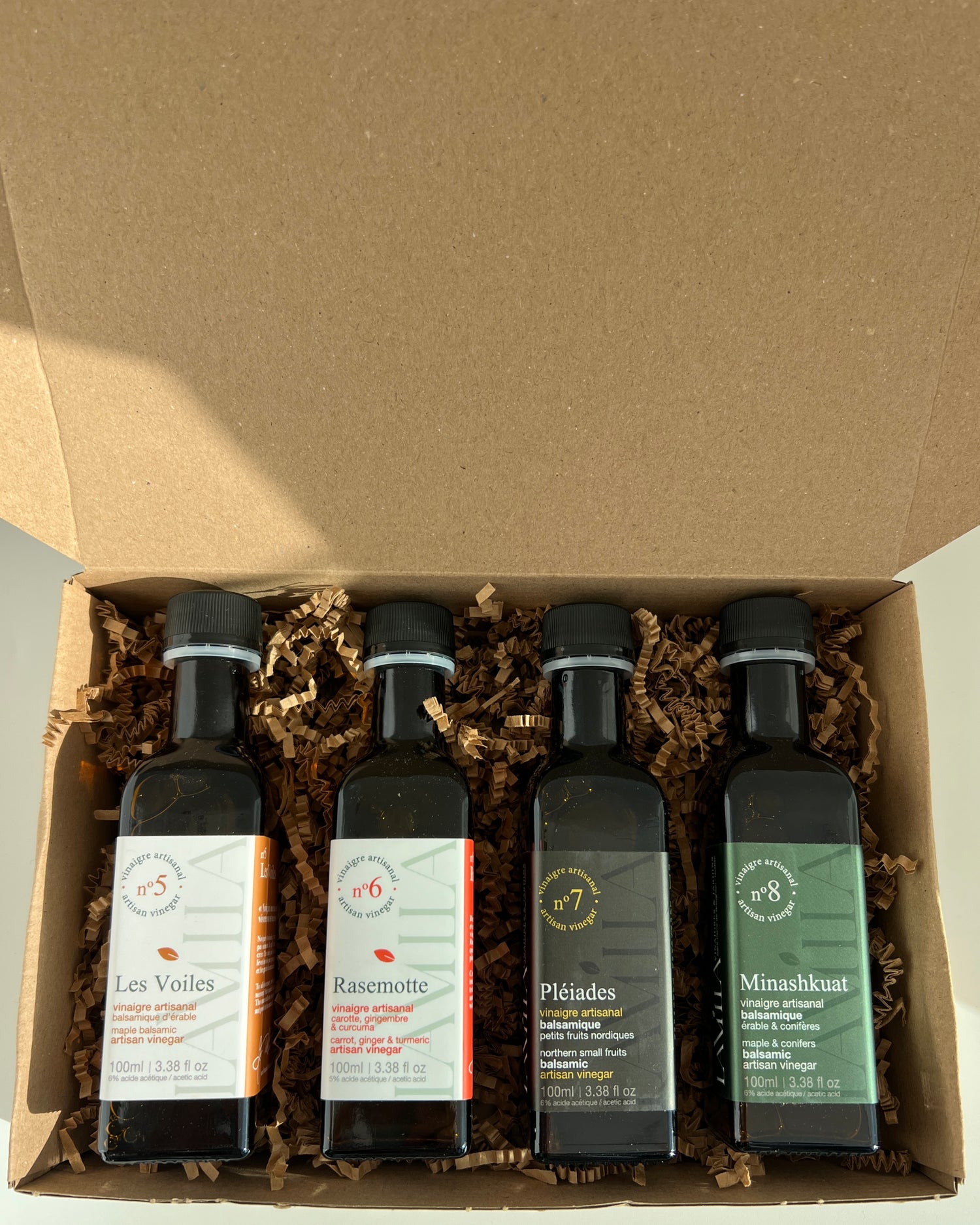 4 side by side bottles of maple vinegars presented in a brown box with straw and sunshine