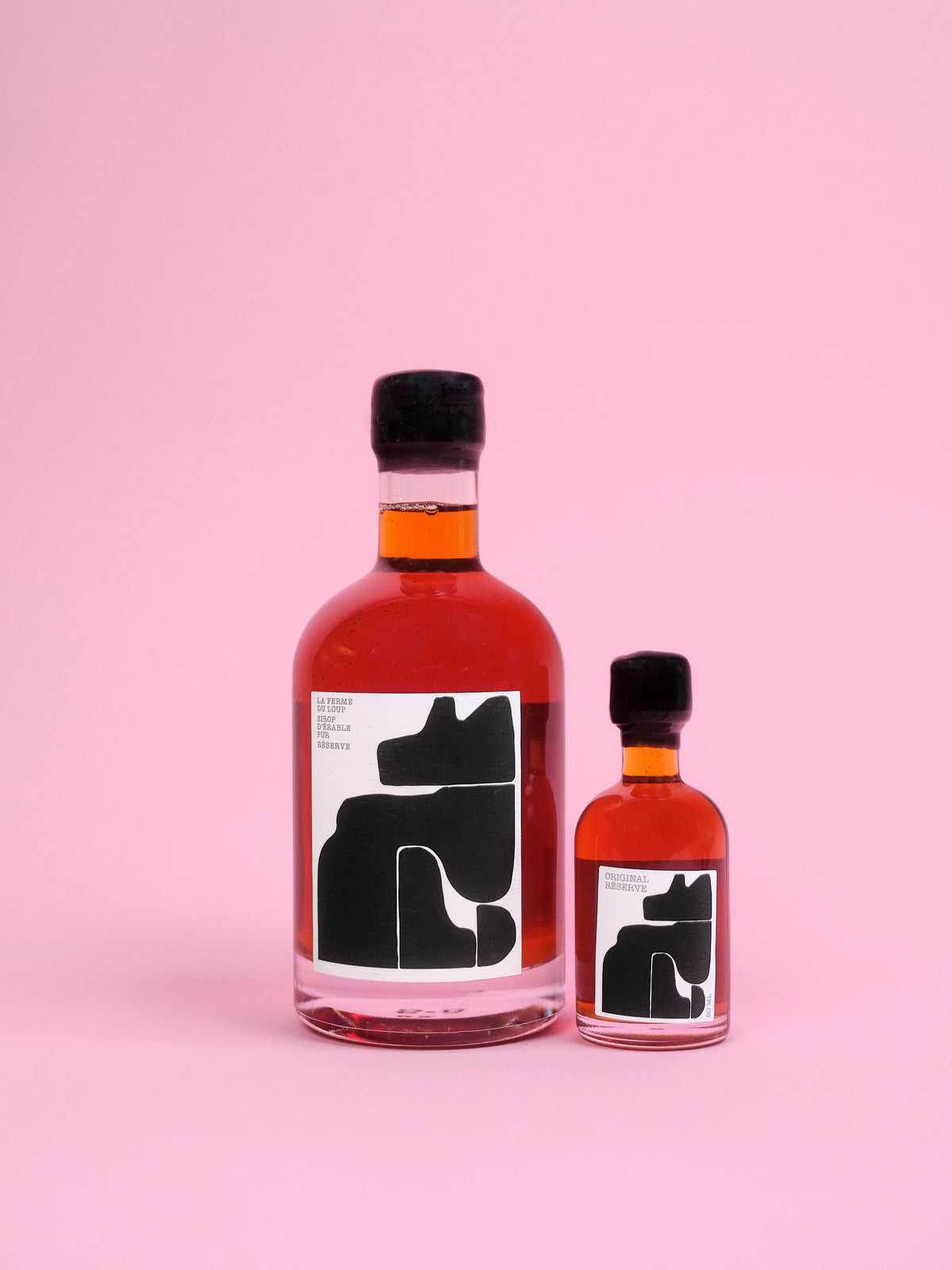 Two bottles of maple syrup with a wolf on a pink background