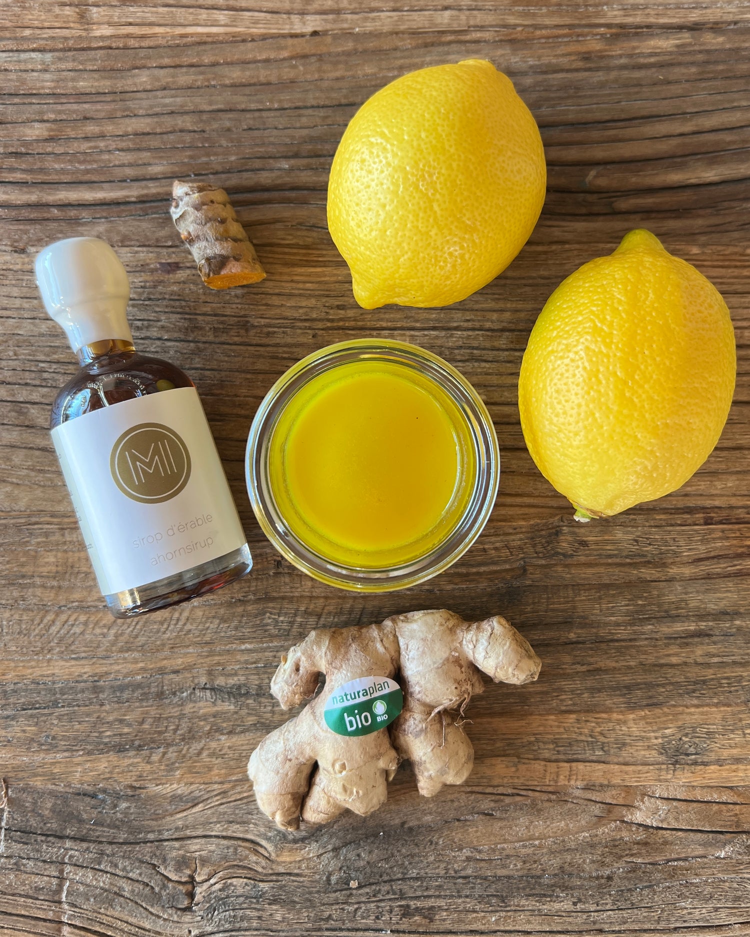 lemons, ginger, turmeric and a bottle of maple syrup with the logo of ME, MAPLE & I on a wood table