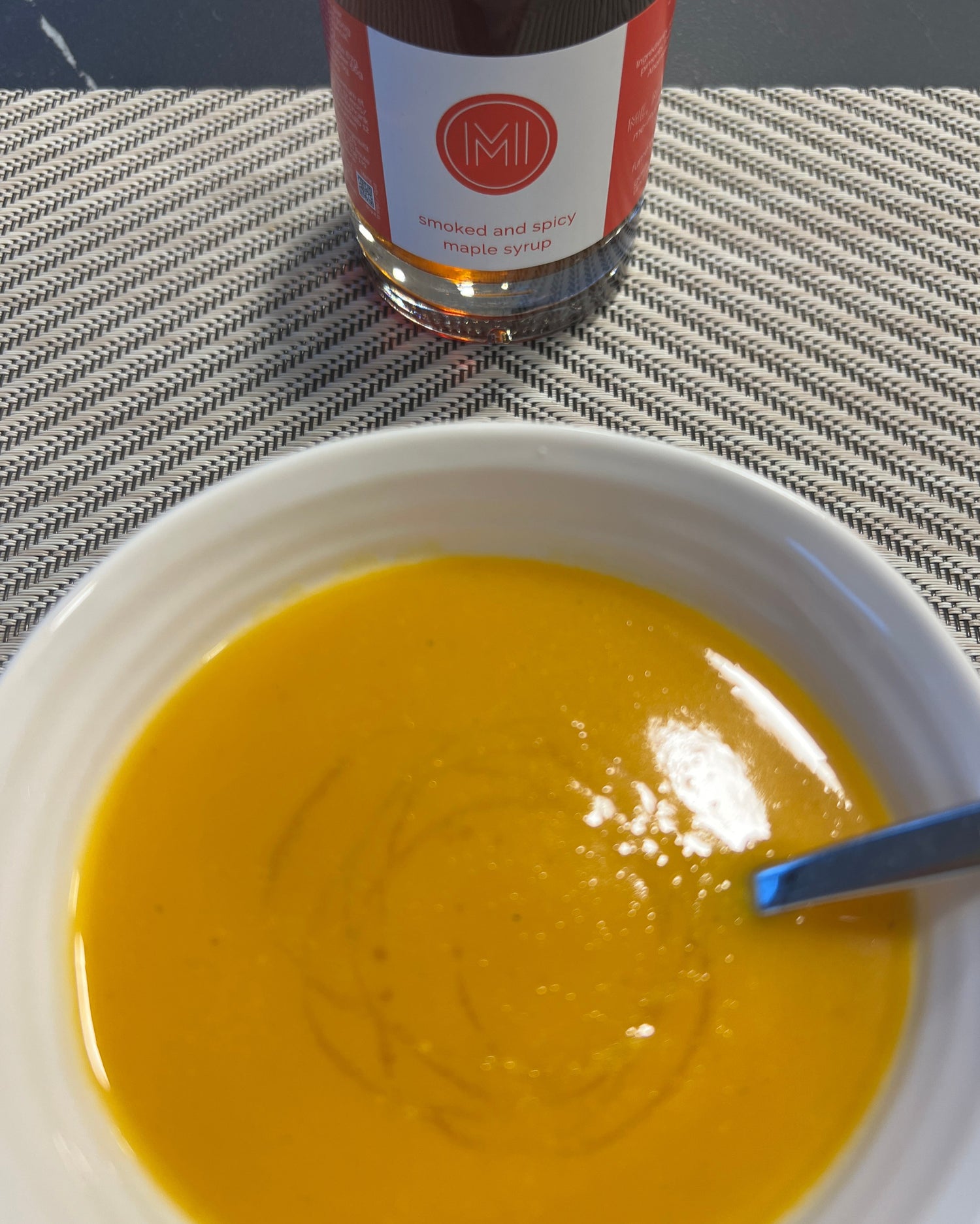 Bowl of maple and butternut quash soup with a maple syrup bottle next to it on a tablecloth