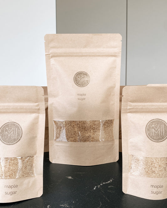 three side by side bags on a grey countertop in two different sizes with see through window showing maple sugar