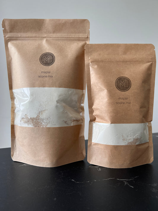 Two paper bags side by side on a countertop with see-through window showing maple scone mix made of maple sugar and flour