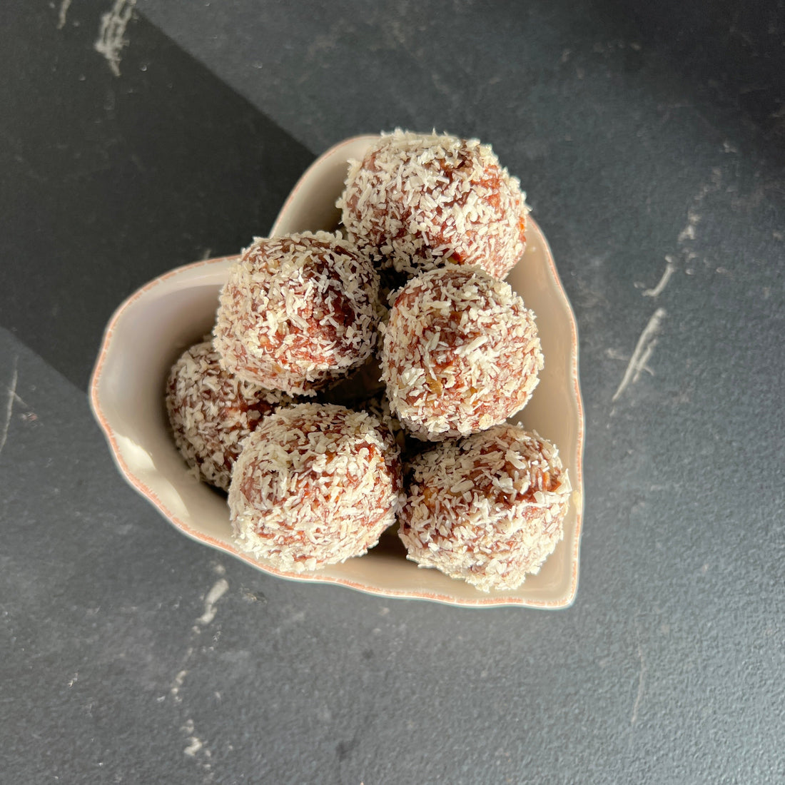 A heart-shape bowl with small brown energy balls on a grey counter