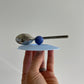 hand holding blue silicon lid with a spoon