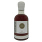 A bottle of dark maple syrup with a white cap and a white label featuring a gold circular logo with the letters 'M' and 'I'.