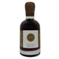 A bottle of coffee-infused maple syrup with a dark brown wooden cap, a white label featuring a gold circular 'MI' logo, and dark brown syrup inside, set against a plain white background.