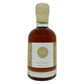 A bottle of vanilla infused maple syrup with amber liquid inside, a white label with a beige logo, and a beige cap, shown on a plain white background.