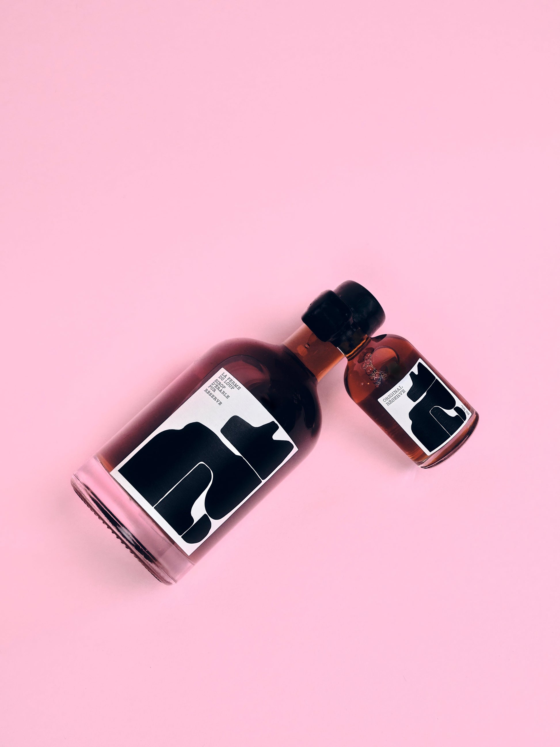 Two bottles of maple syrup with a wolf laying on a pink background