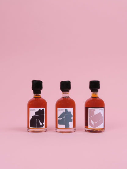Three small bottles with black caps and labels on a pink background