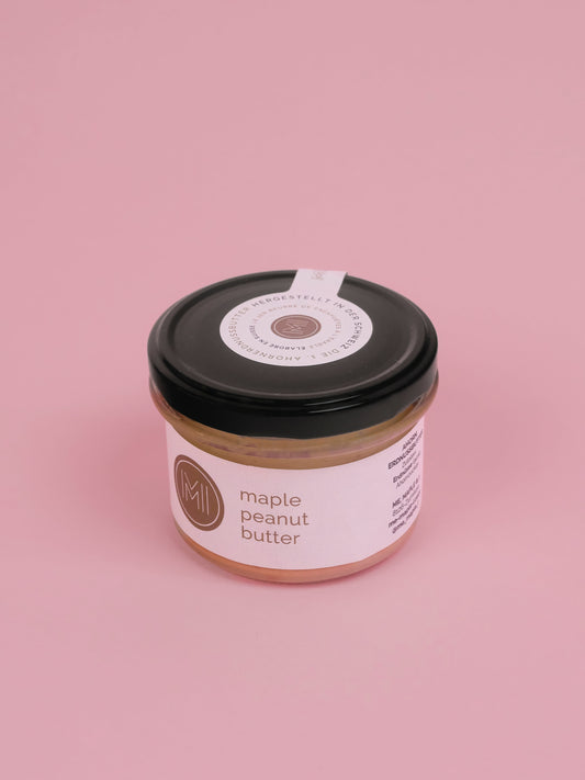 A jar of maple peanut butter taken from the top on a pink background