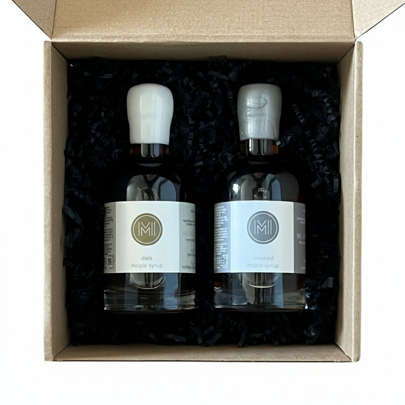 Two bottles of maple syrup in a cardboard box on a wooden surface
