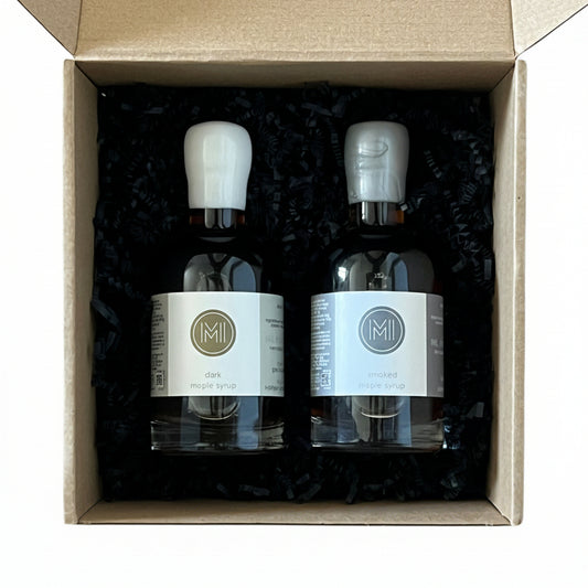 Two bottles of maple syrup in a cardboard box on a wooden surface