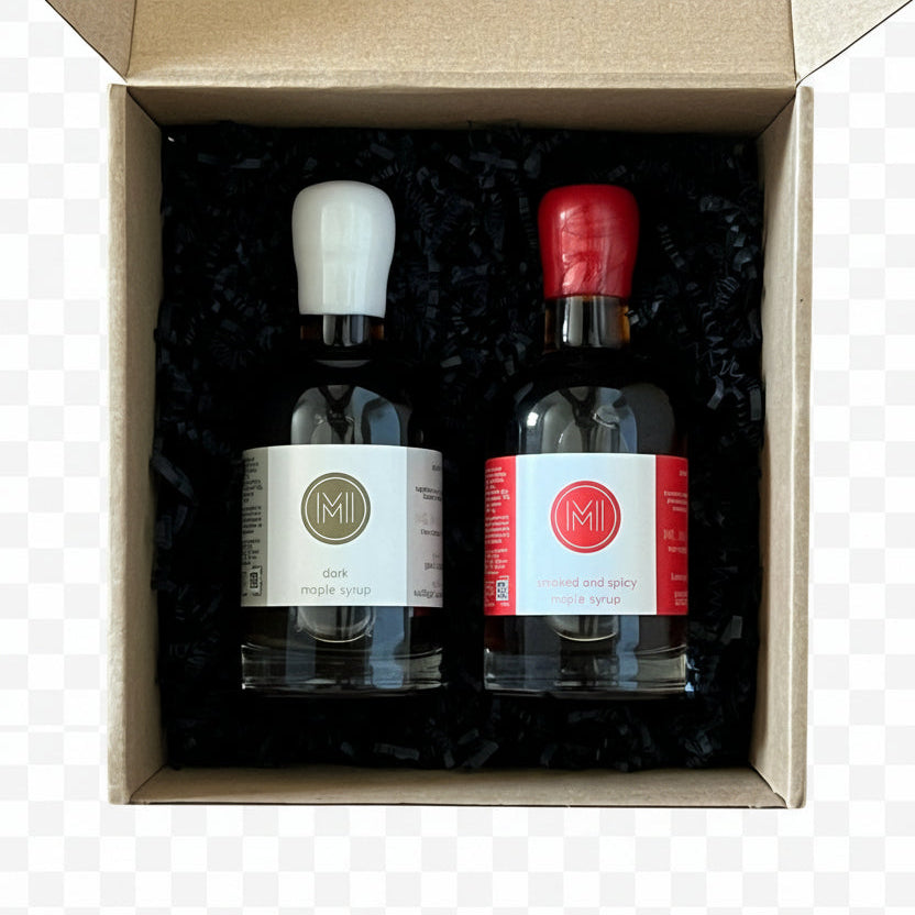 Two bottles of maple syrup in a cardboard box on a wooden surface
