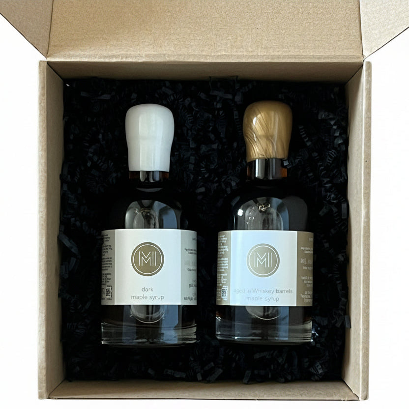Two bottles of maple syrup in a cardboard box on a wooden surface
