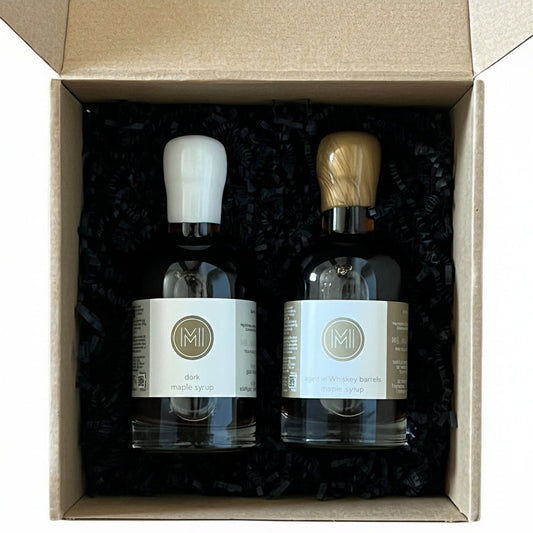 Two bottles of maple syrup in a cardboard box on a wooden surface