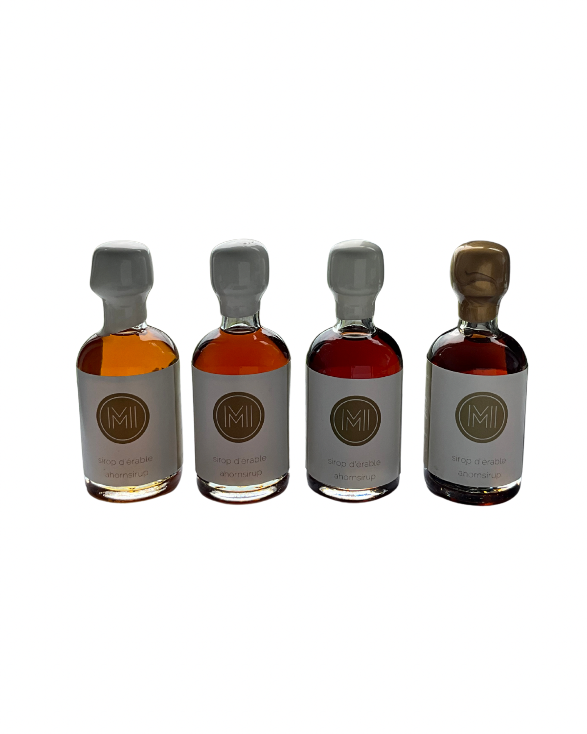 4x50ml side by side bottles of golden, amber, dark and whiskey maple syrup  standing with no background