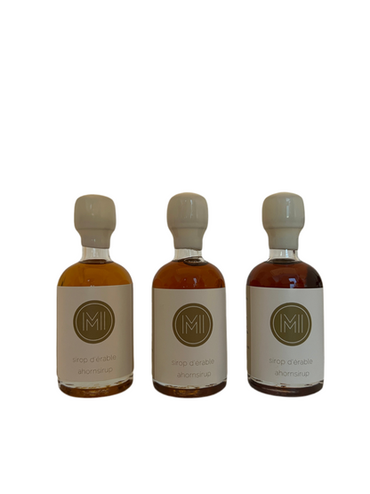 3x50ml side by side bottles of golden, amber and dark maple syrup standing with no background