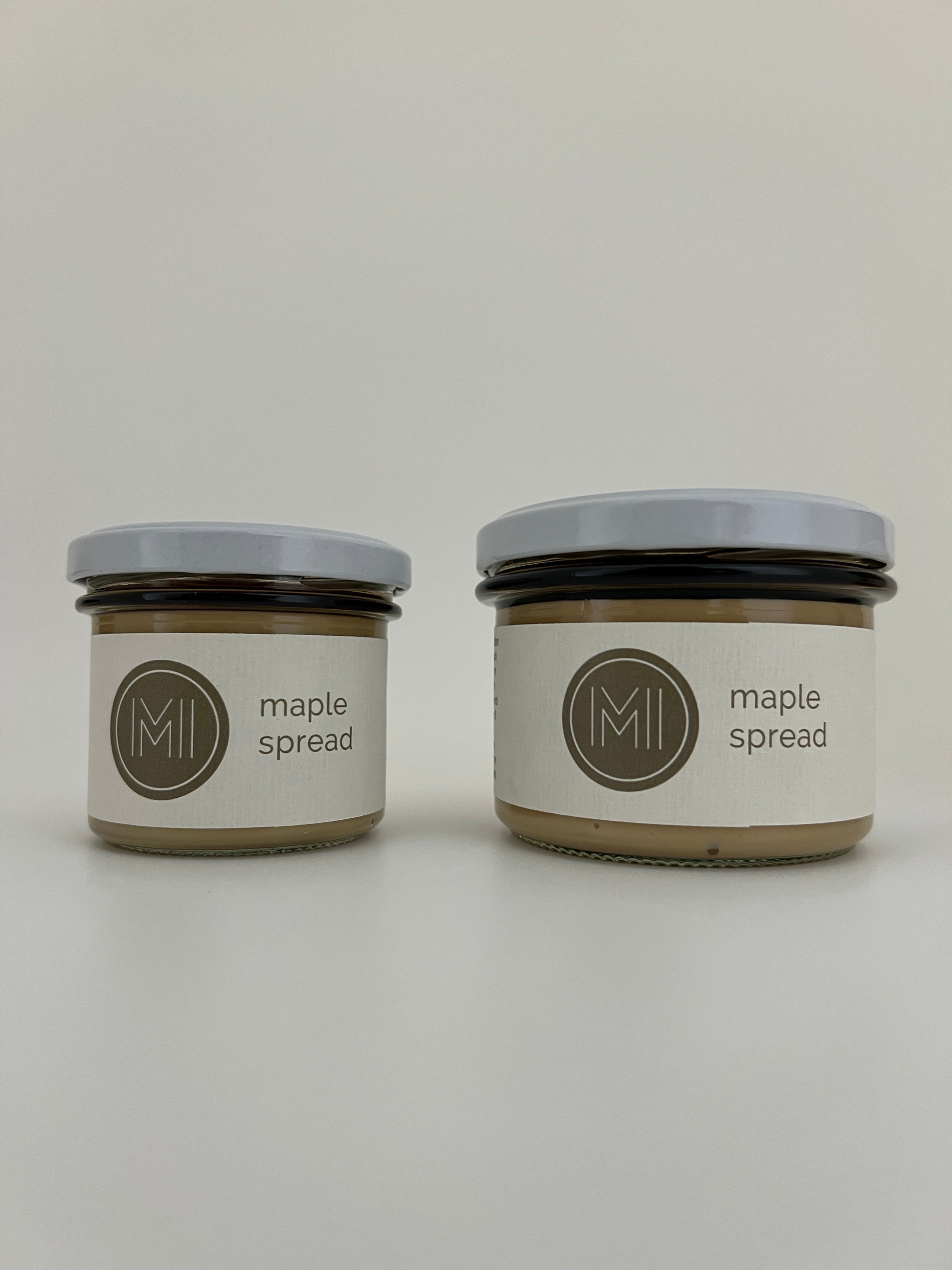 a small size and a medium size maple spread jars with white lids side by side on a white background