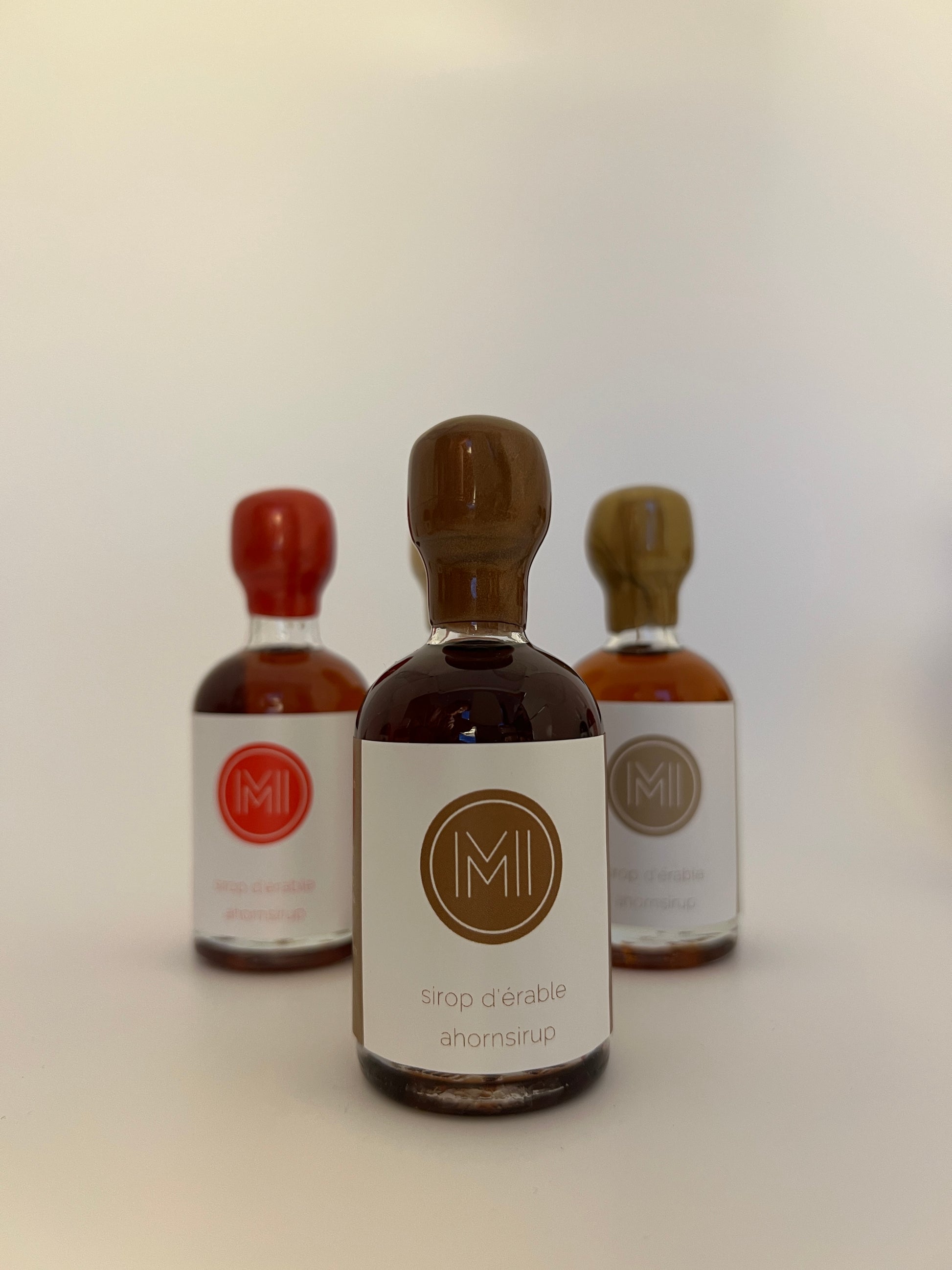 a 50 ml bottle of coffee infused maple syrup with a brown wax seal  in front of 2 other bottles of the same style but different colors on a white 