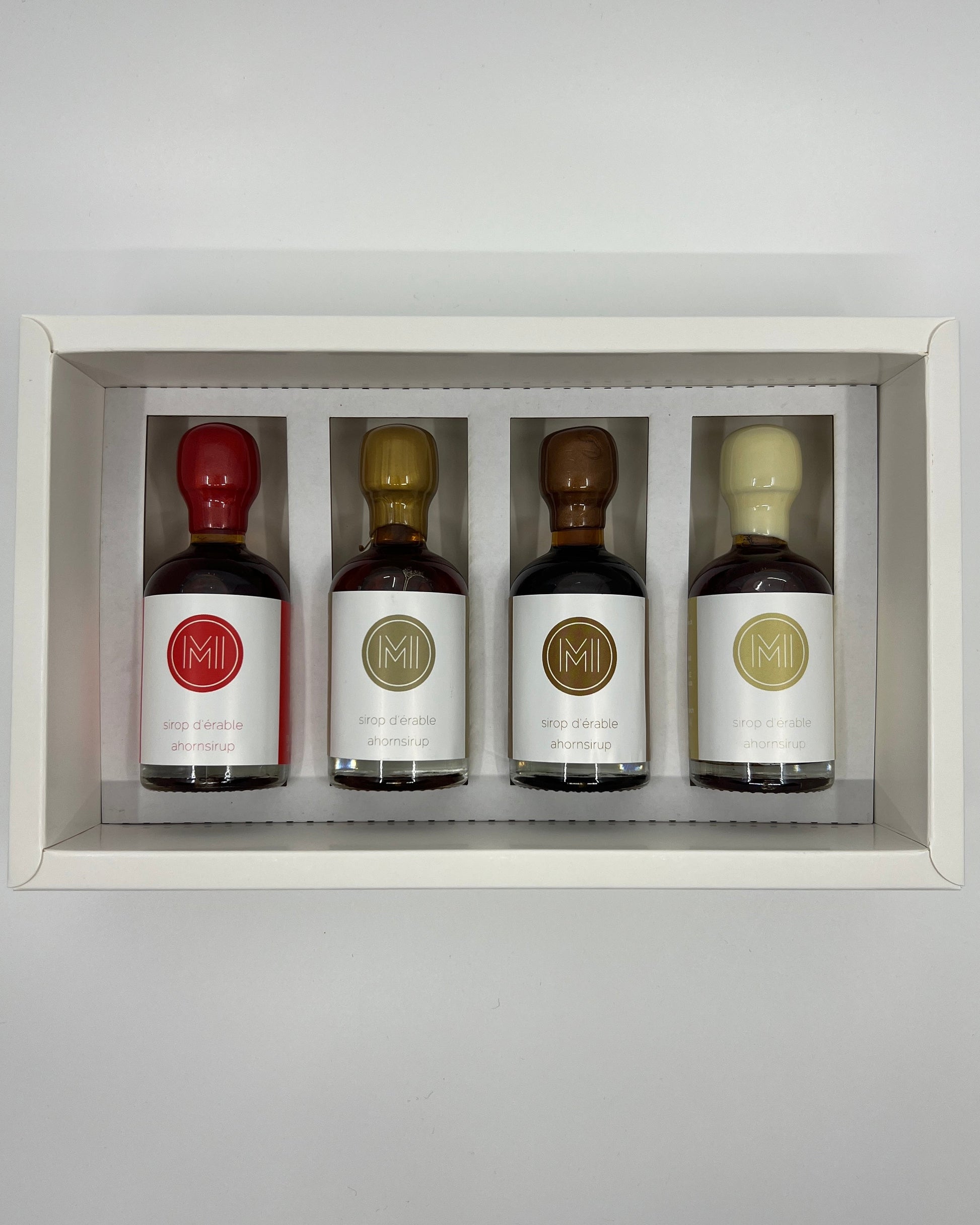 4 side by side small bottles of maple syrup presented in a white box with insert on a white background