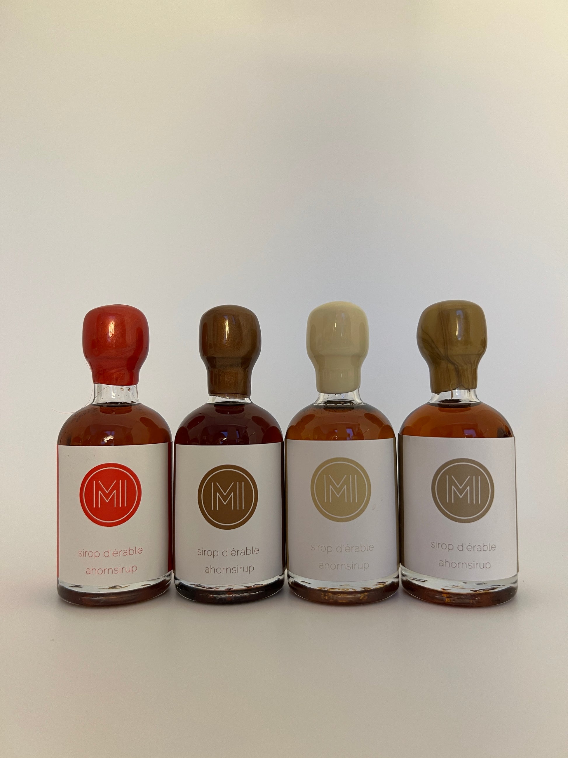 4 small bottles of maple syrup with different seals and logo  aligned on a white background