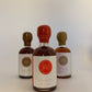 a 50 ml bottle of spicy maple syrup with a red wax seal in front of 2 other bottles of the same style but different colors on a white background.