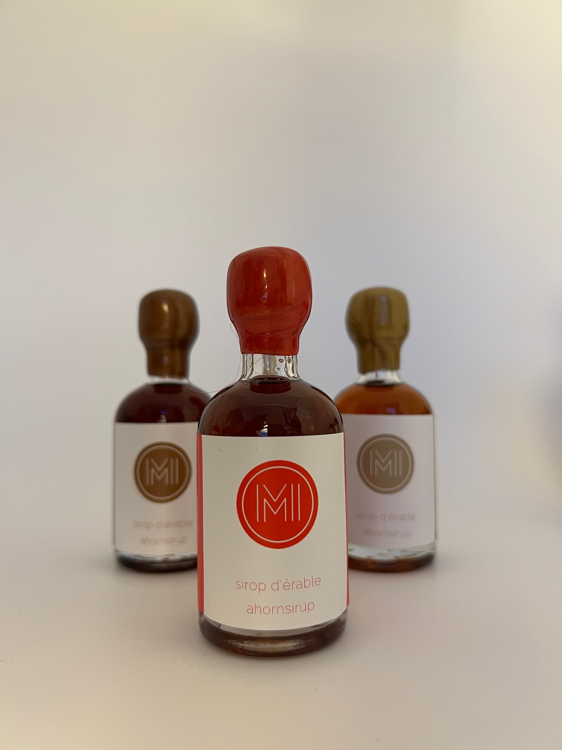 a 50 ml bottle of spicy maple syrup with a red wax seal in front of 2 other bottles of the same style but different colors on a white background.