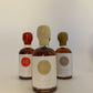 a 50 ml bottle of vanilla infused maple syrup with a beige wax seal  in front of 2 other bottles of the same style but different colors on a white 