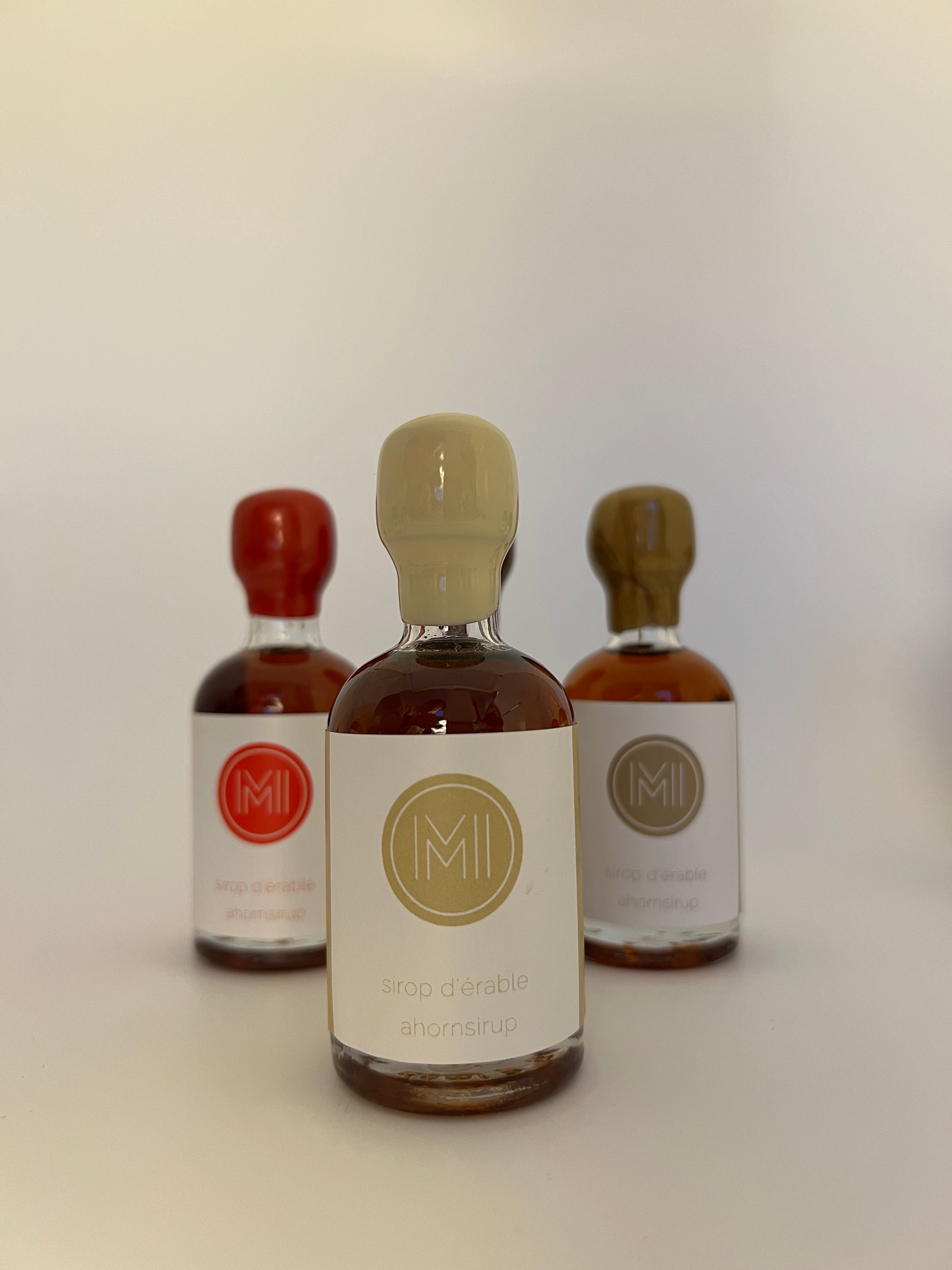a 50 ml bottle of vanilla infused maple syrup with a beige wax seal  in front of 2 other bottles of the same style but different colors on a white 