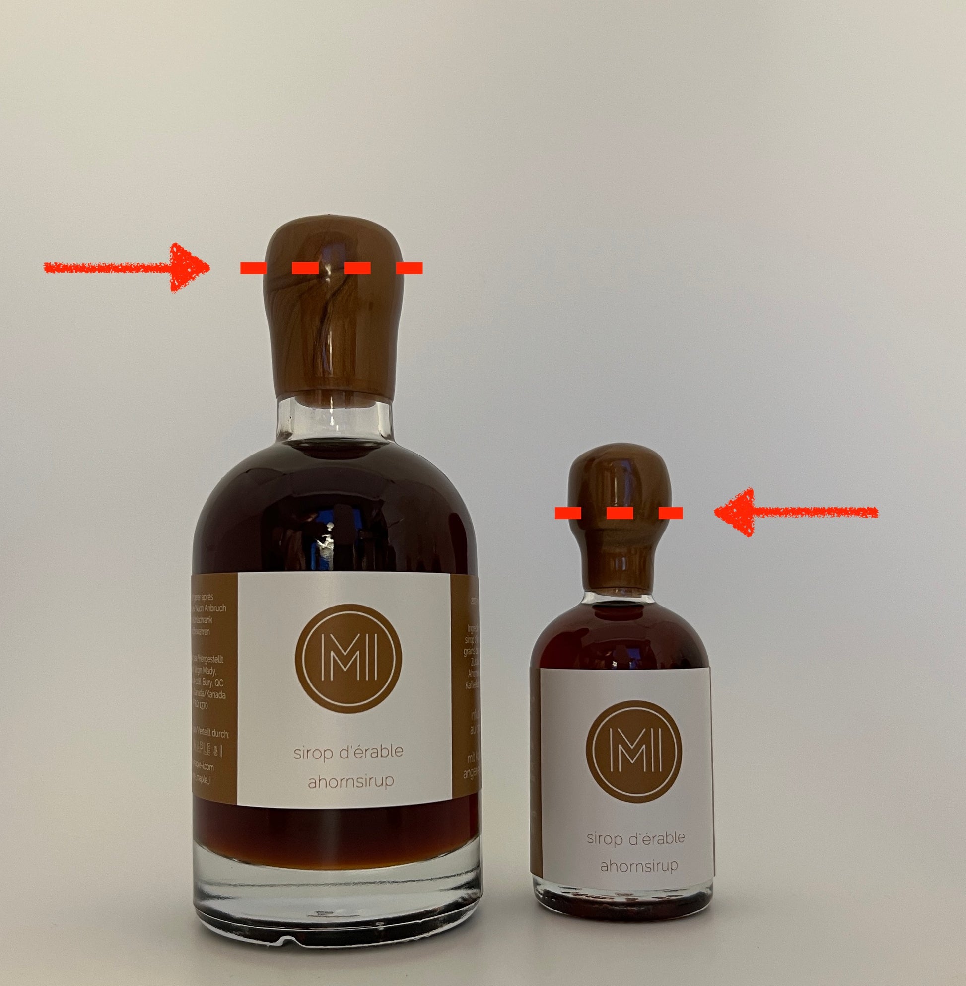 2 bottles of maple syrup with a brown wax and red lines and arrow to show where to cut the wax to open the bottle