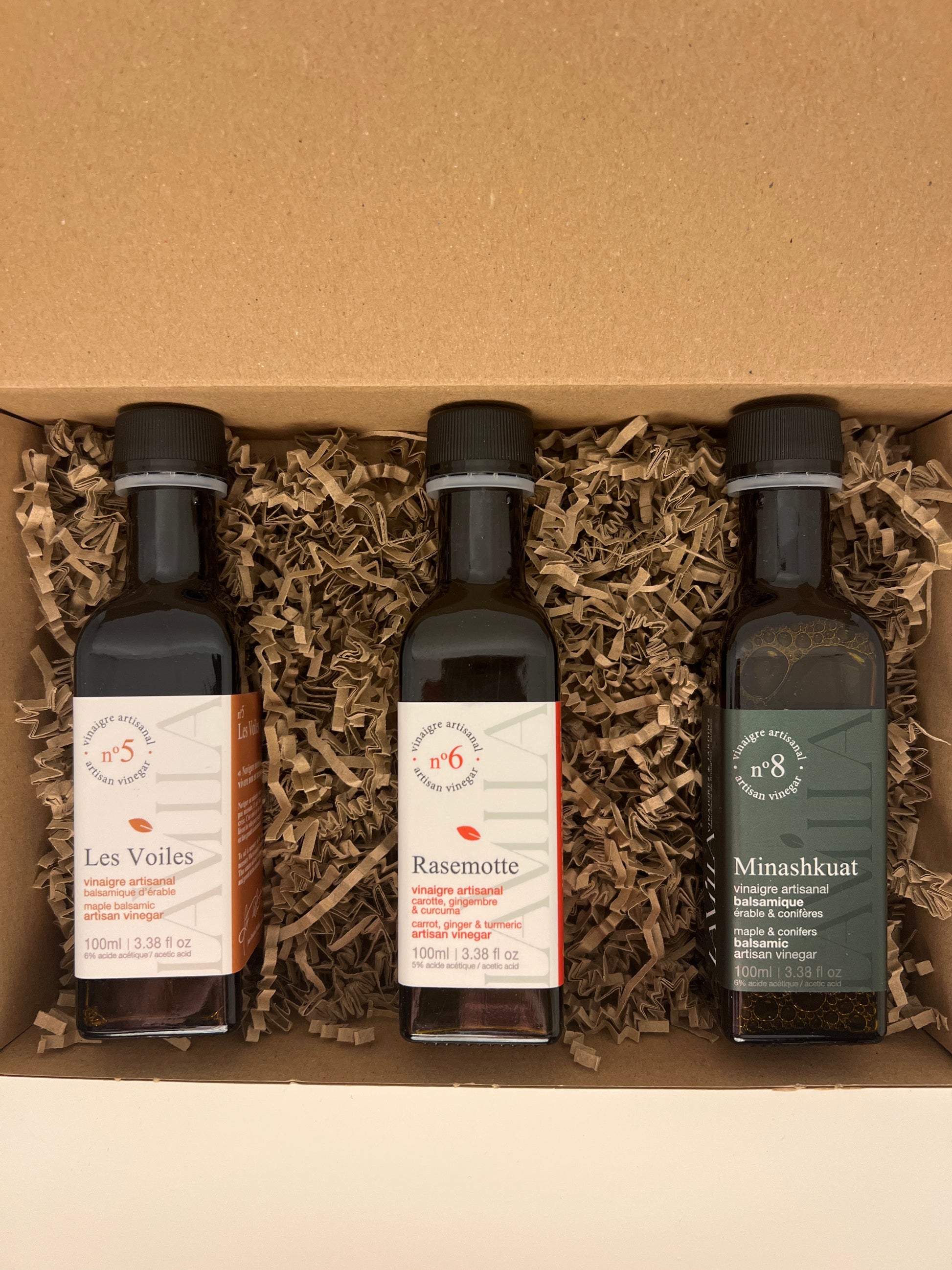3 side by side bottles of maple vinegars presented in a brown box with straw 