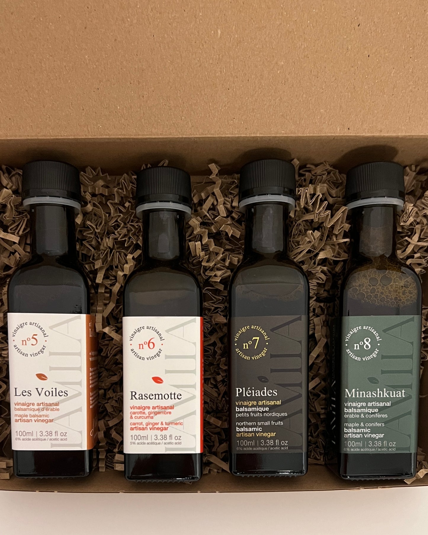 4 side by side bottles of maple vinegars presented in a brown box with straw 