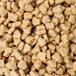 A close-up, top-down view of numerous small, light tan, soft maple candy or fondants piled together.