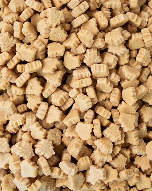 A close-up, top-down view of numerous small, light tan, soft maple candy or fondants piled together.