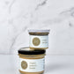 A jar of maple spread on top of a maple peanut butter on a white marble background