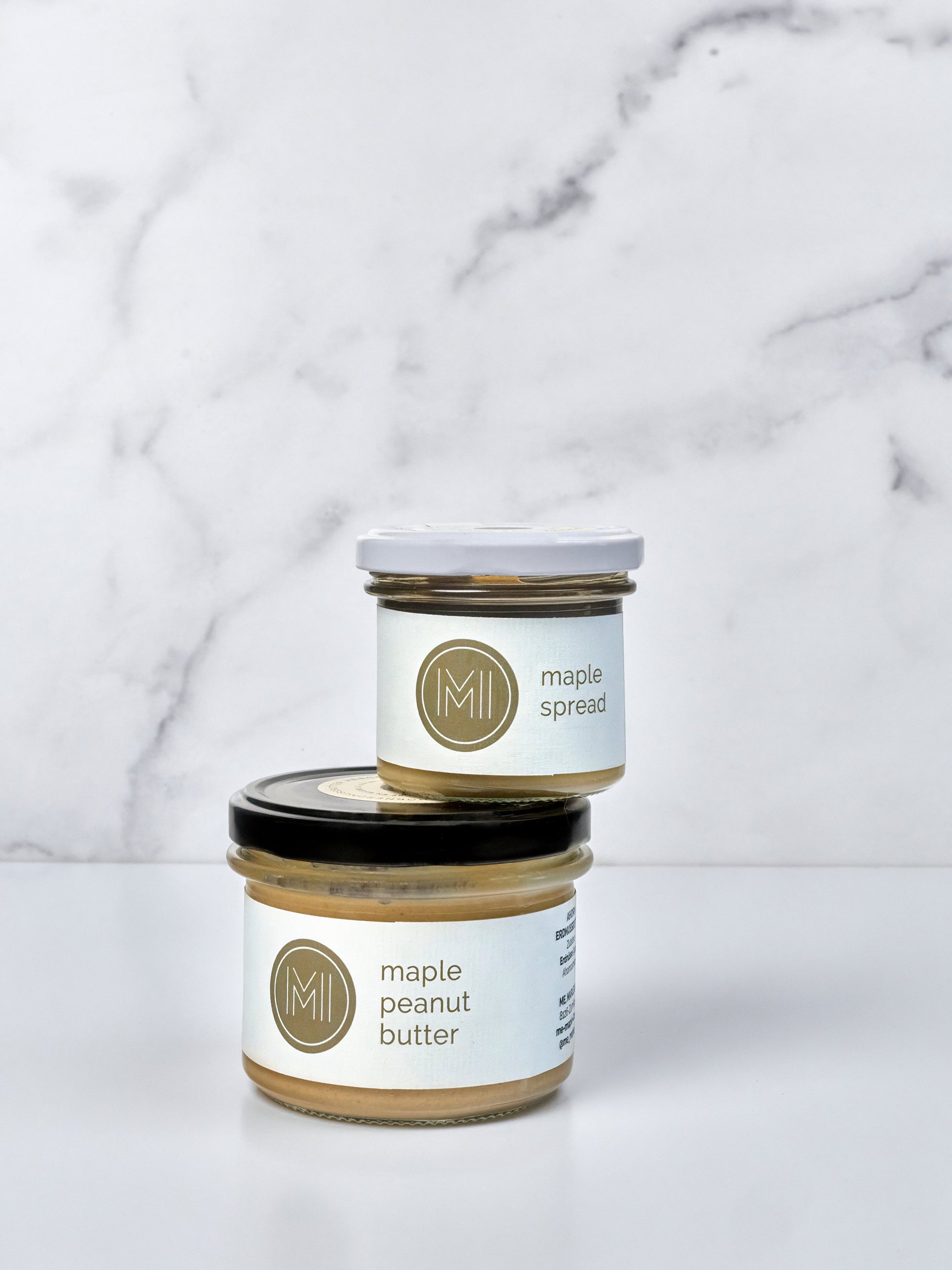 A jar of maple spread on top of a maple peanut butter on a white marble background