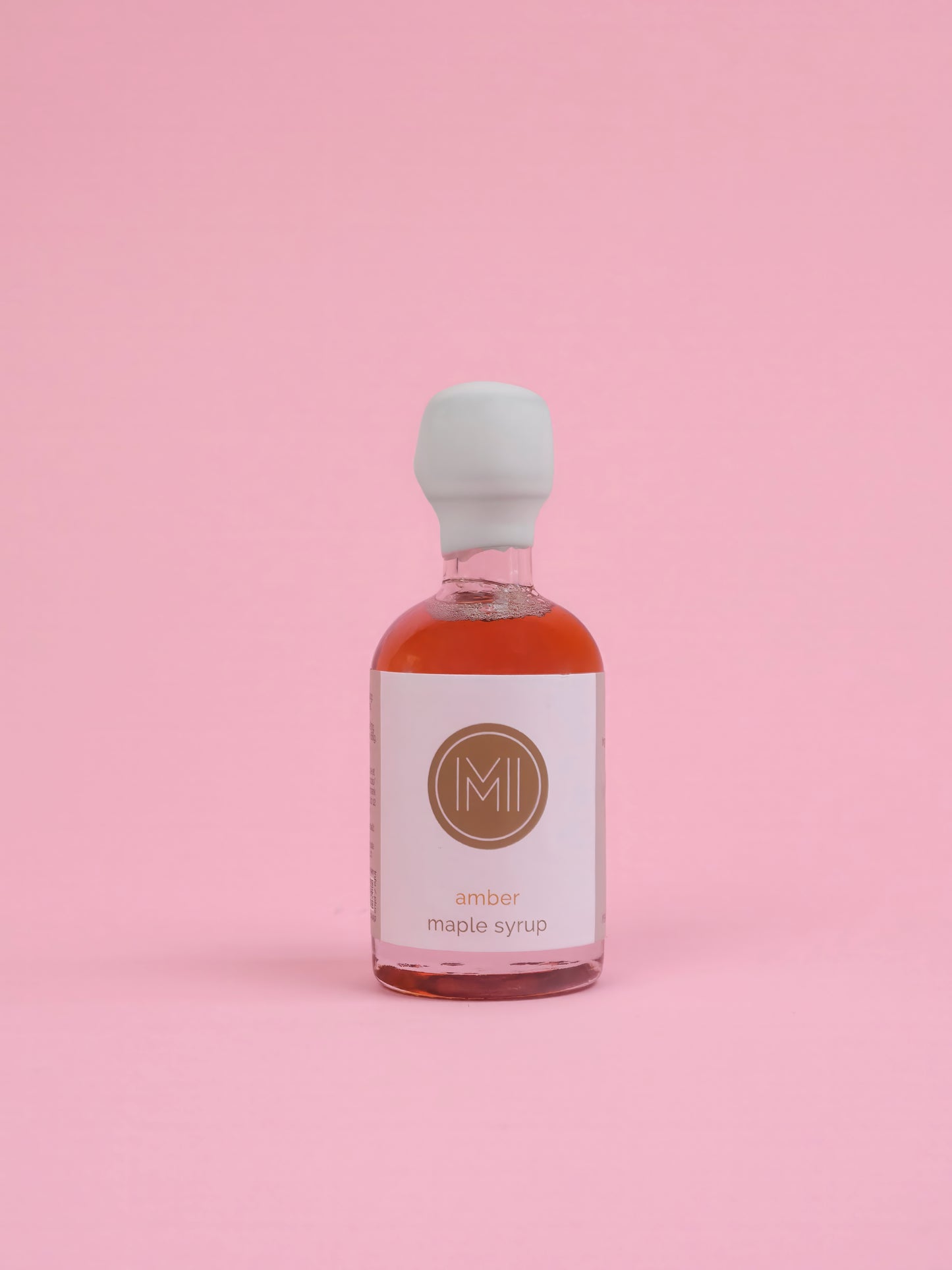 Bottle of amber maple syrup with a white label on a pink background