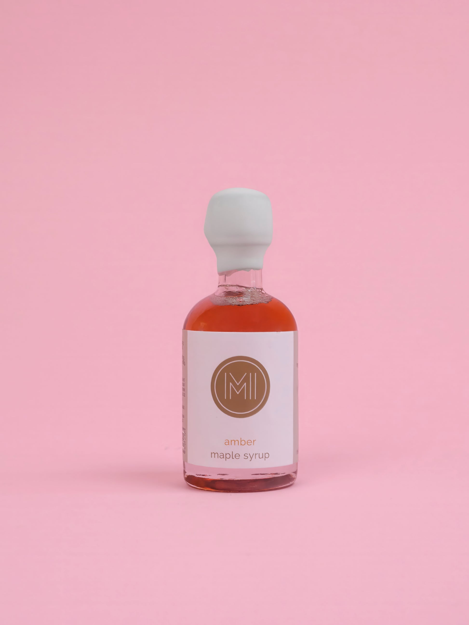 Bottle of amber maple syrup with a white label on a pink background