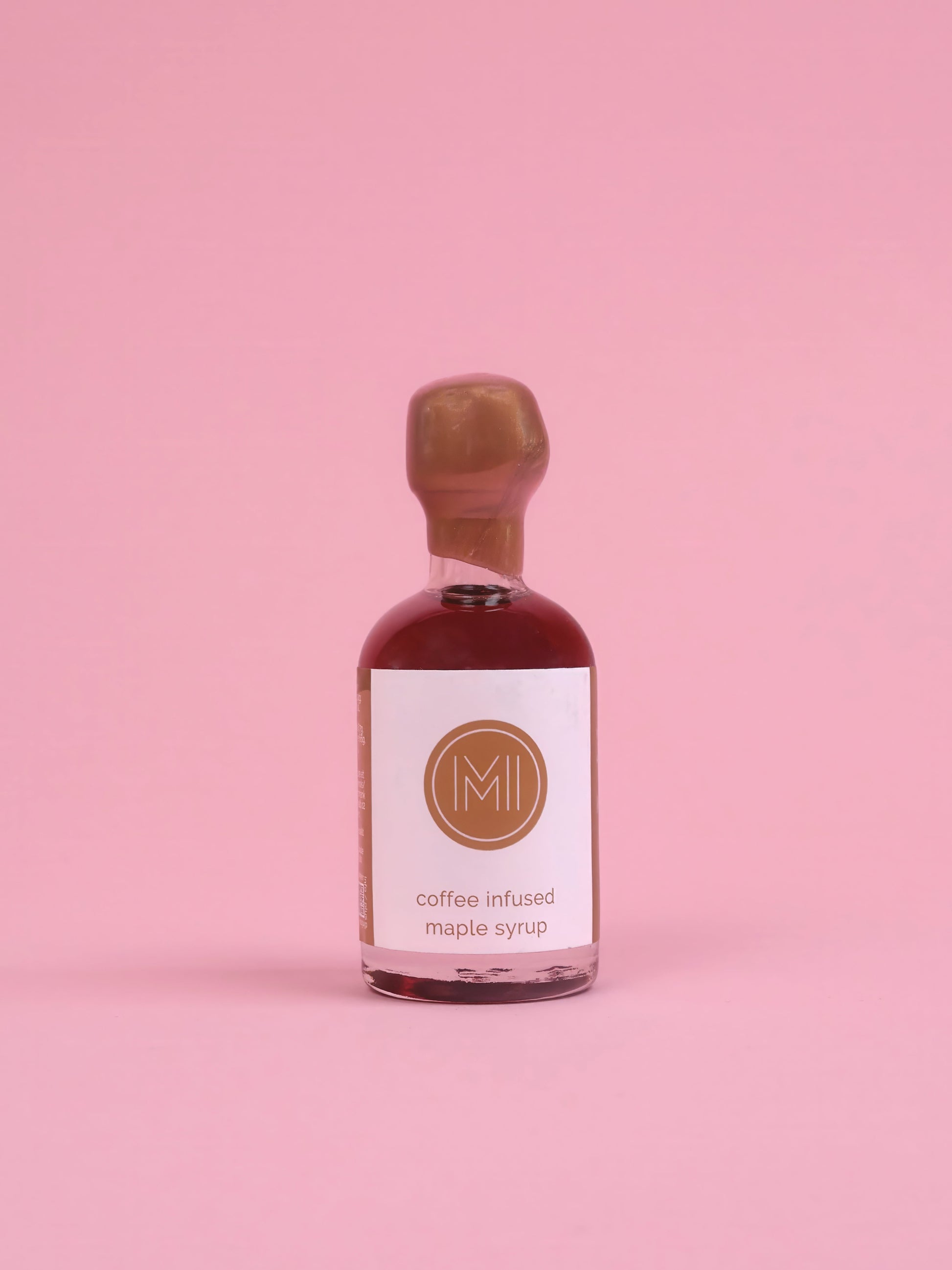 Bottle of coffee-infused maple syrup with a white label on a pink background