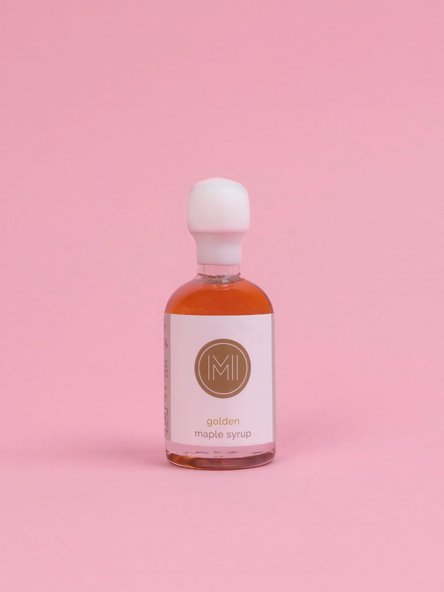 Bottle of golden maple syrup with a white label on a pink background