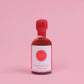 Bottle of smoked and spicy maple syrup with a red cap on a pink background