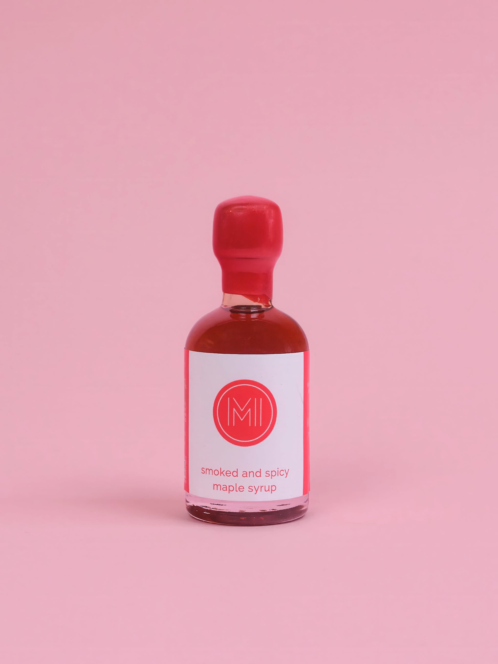 Bottle of smoked and spicy maple syrup with a red cap on a pink background