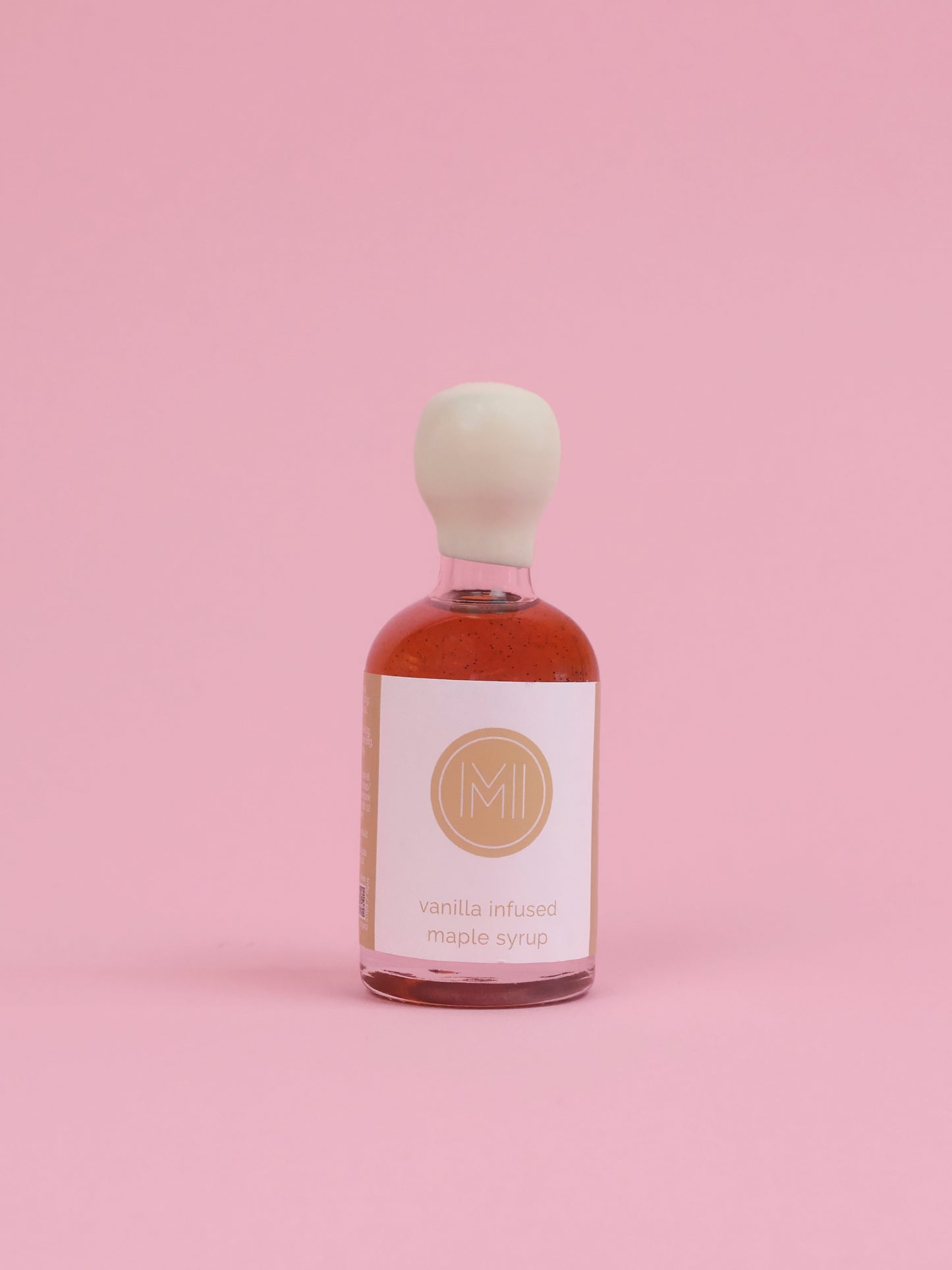 Bottle of vanilla infused maple syrup with a white label on a pink background