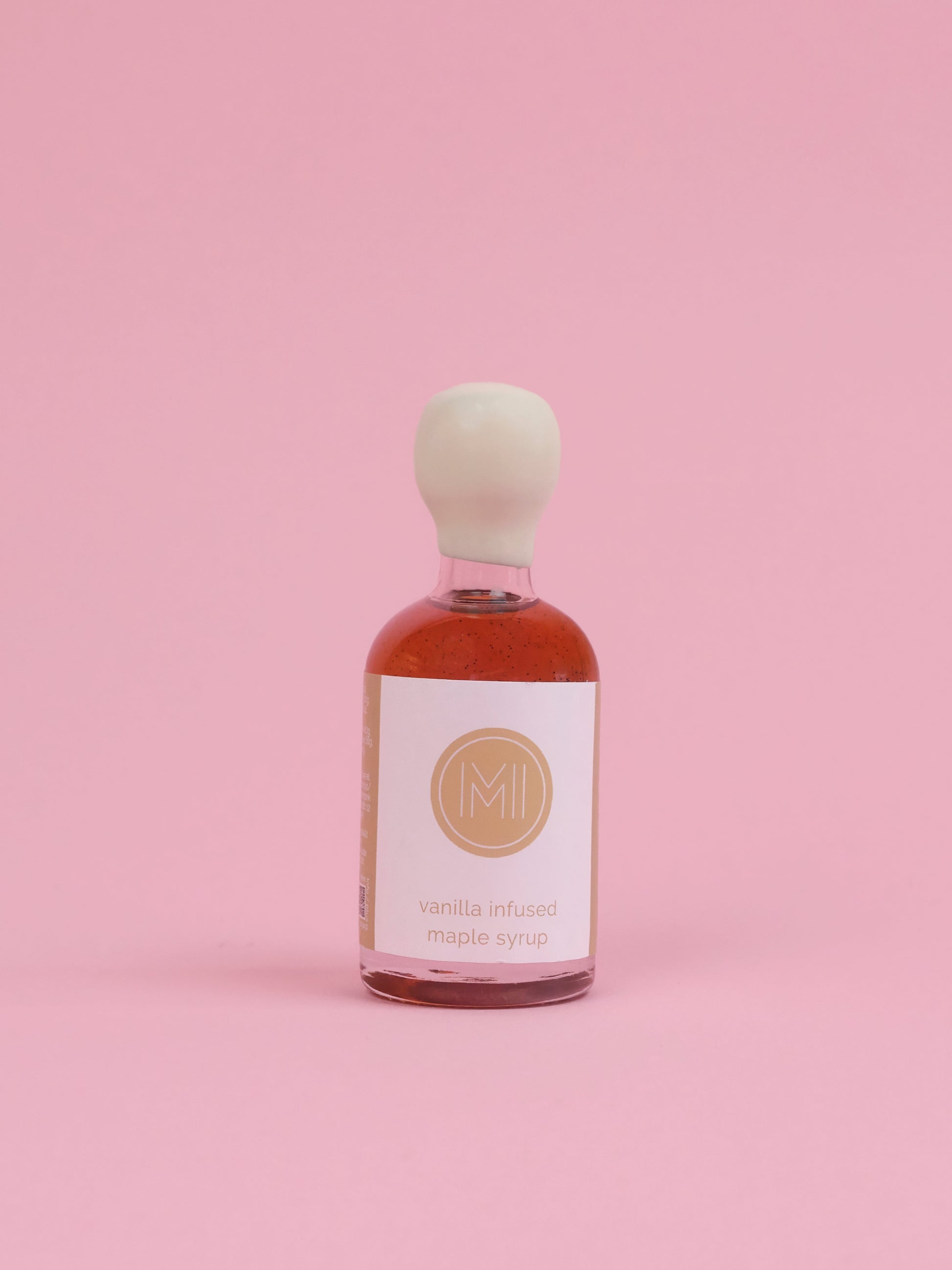 Bottle of vanilla infused maple syrup with a white label on a pink background